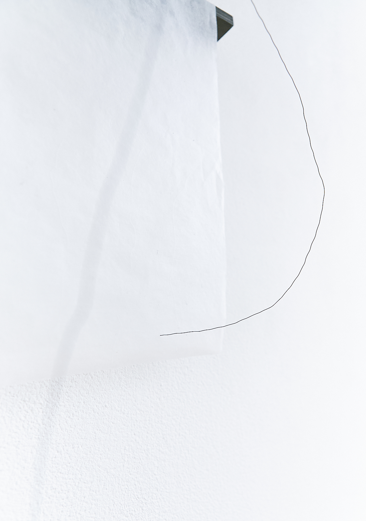 a black wire line running across a white wall with a piece of black wood in the top right corner
