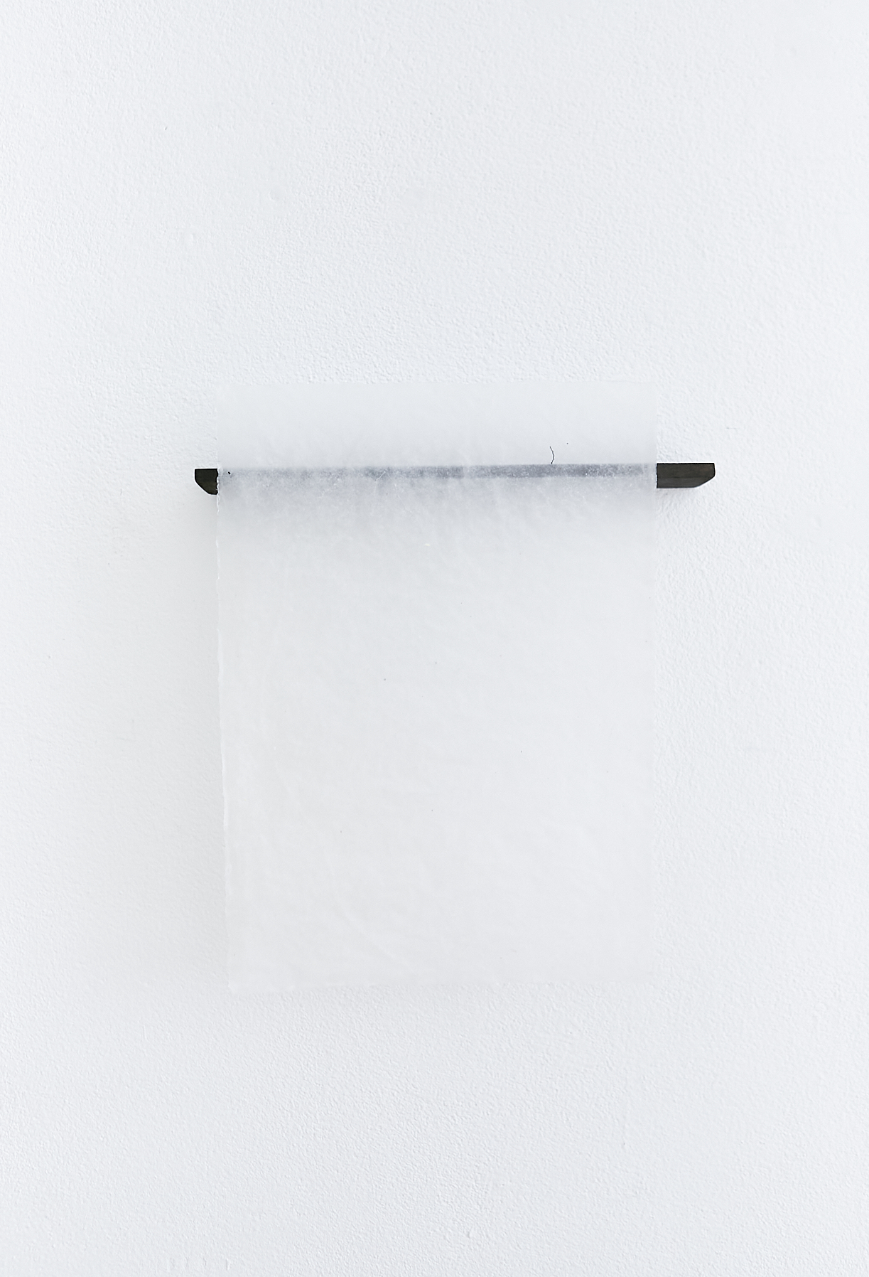 a black piece off wood with a transparent handmade paper over it is haning off a white wall