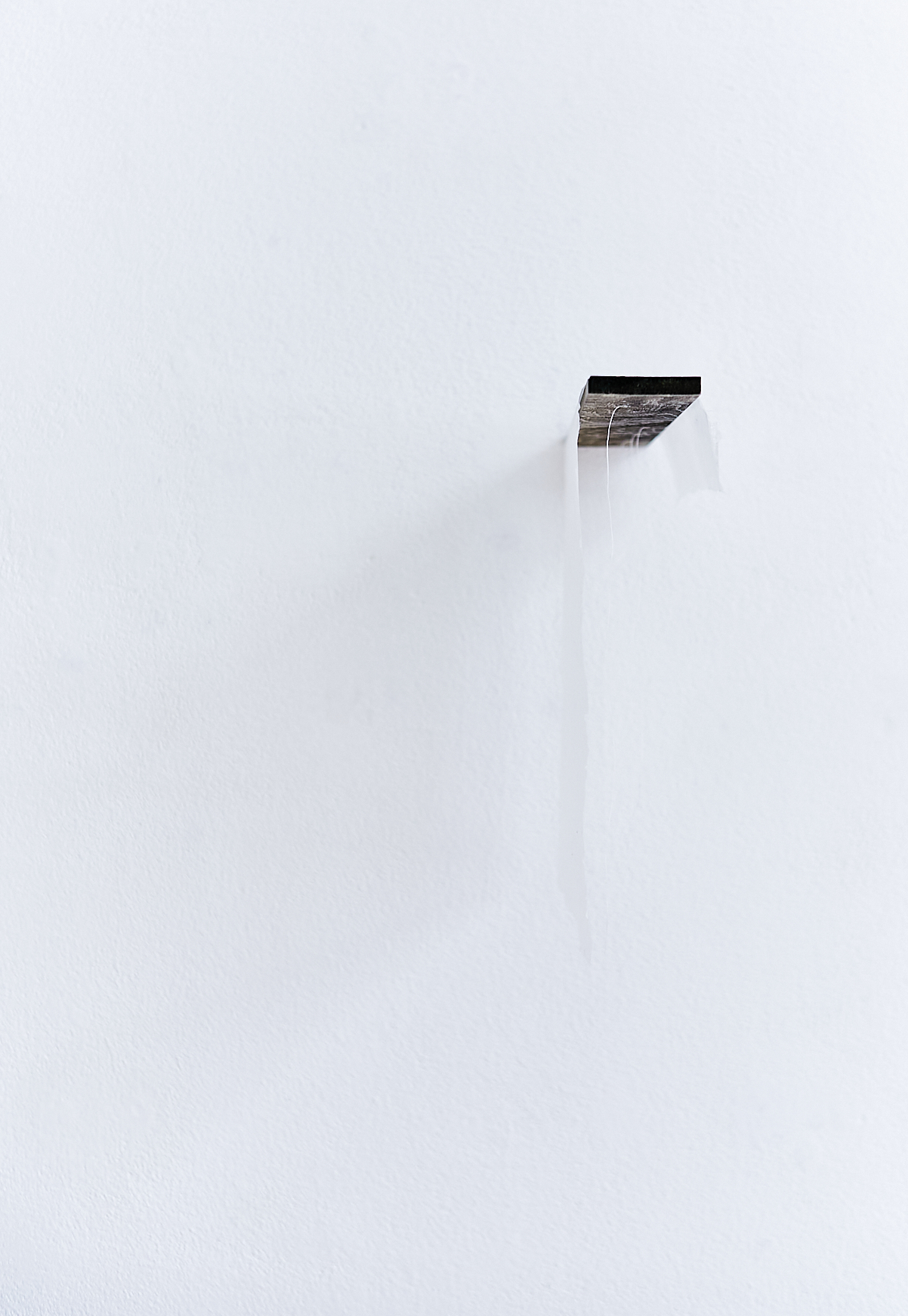 a piece of dark brown wood hanging off a white wall. A white handmade paper hangs over the wood as well as some white strings