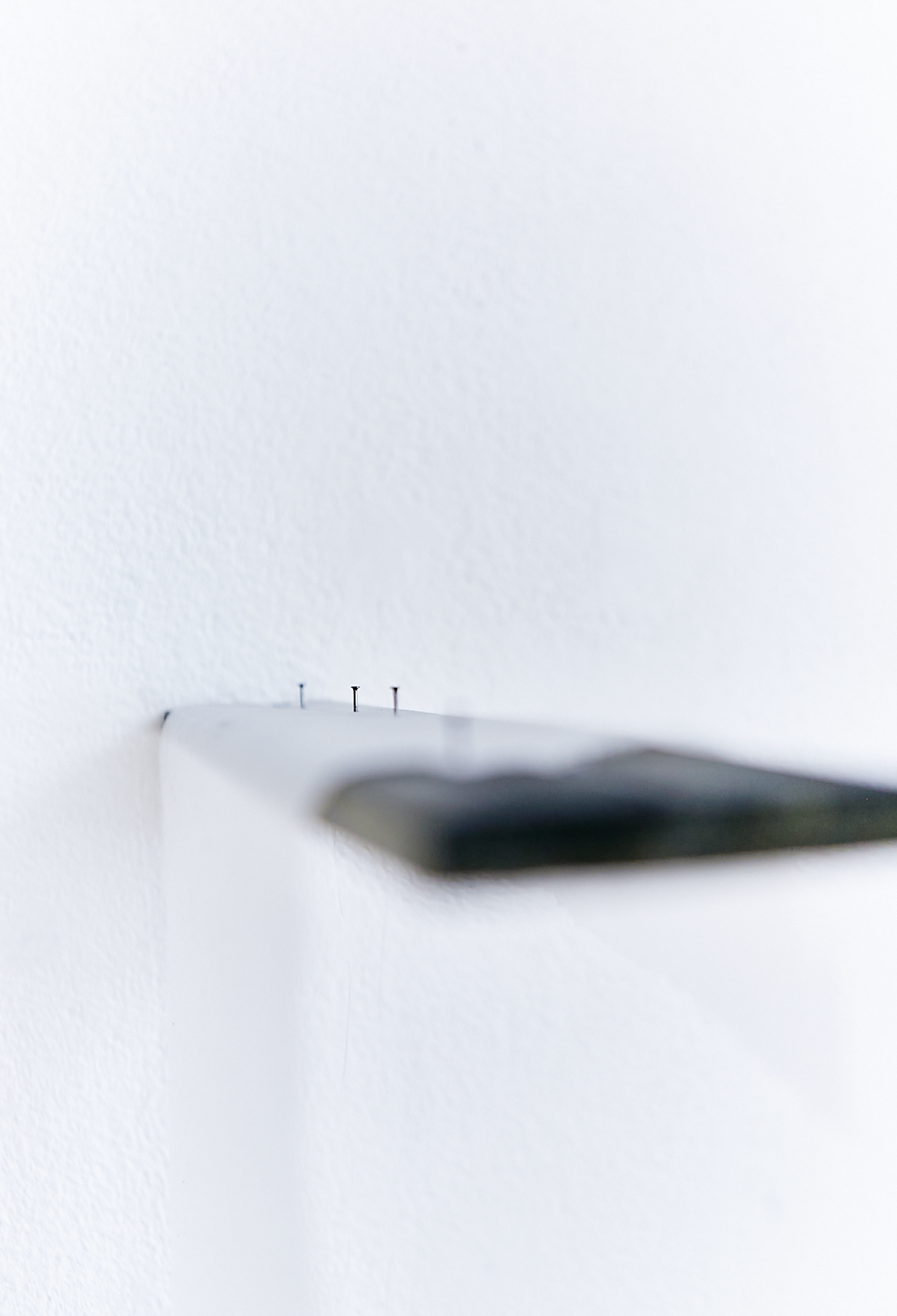 a dark brown wooden board hanging off a white wall. Three steel nails attached on the wood with a white handmade paper