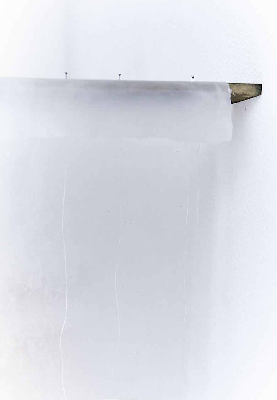 a dark brown wooden board hanging off a white wall. Three steel nails attached on the wood with a white handmade paper. Three bright white lines are running vertically down the image