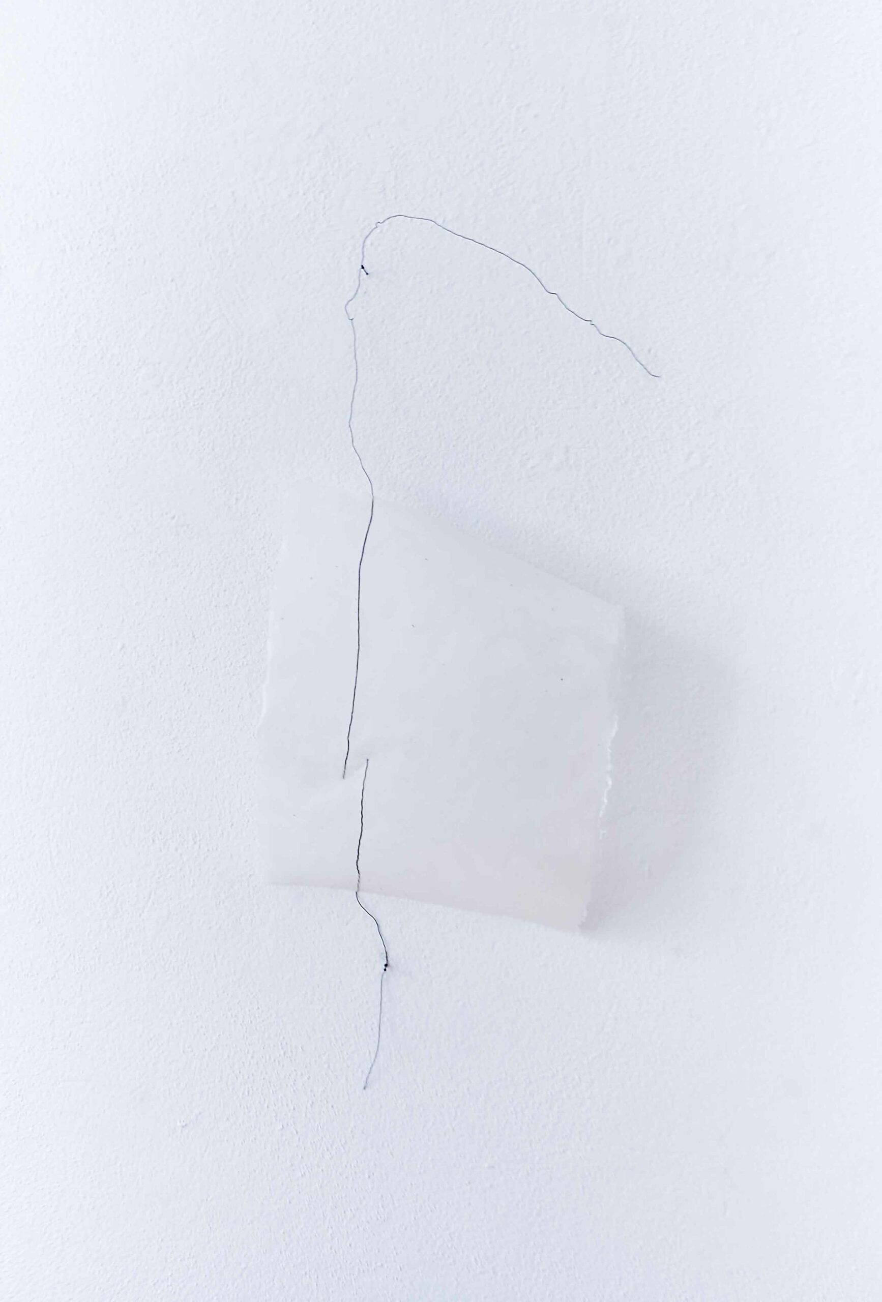 two black wire lines running across a bended white handmade paper off a white wall