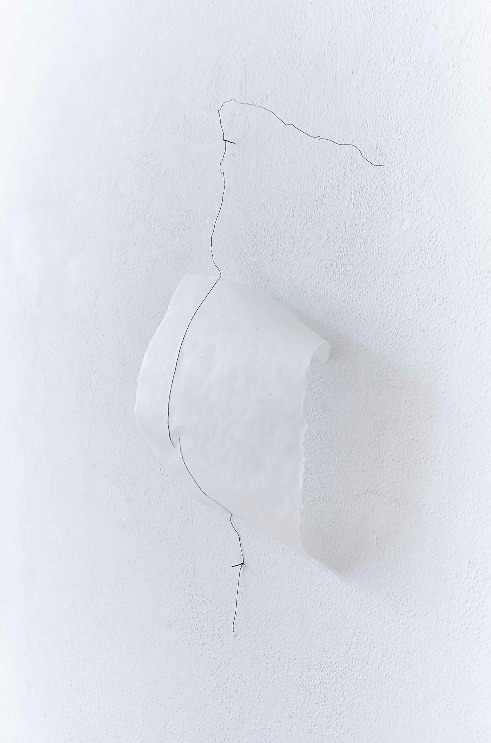 two black wire lines running across a bended white handmade paper off a white wall