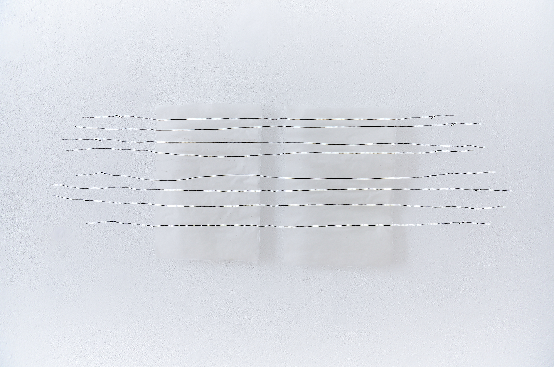 two handmade white papers installed on a white wall with eight black wire lines running across them, attached to nails in the wall