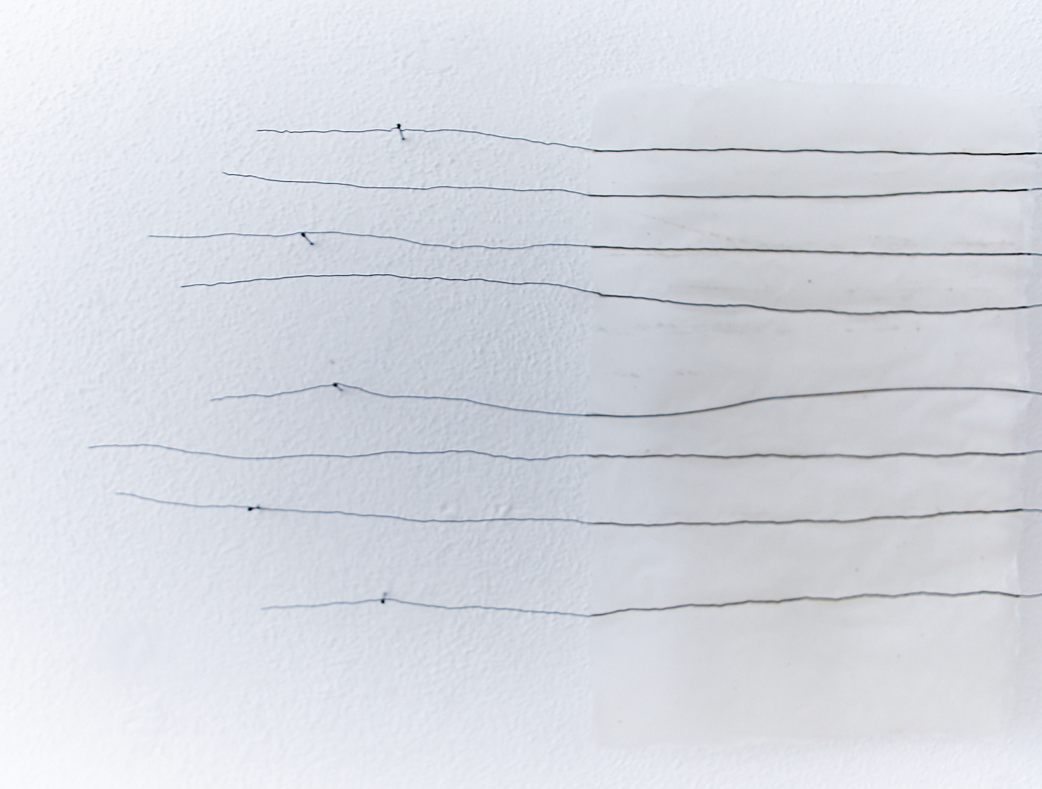 eight black wire lines wrapped around nailheads placed in a white handmade paper installation on white wall