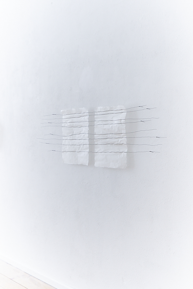 two handmade white papers installed on a white wall with eight black wire lines running across them, attached to nails in the wall