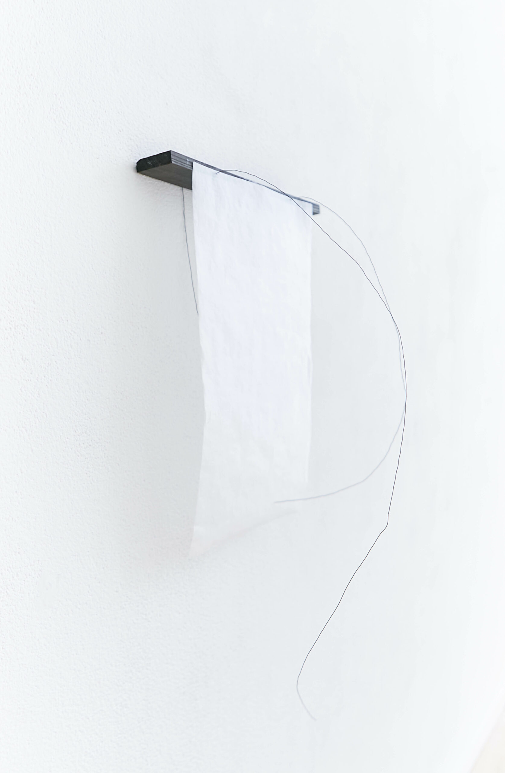 a black piece off wood with a transparent handmade paper over it is hanging off a white wall with three black wire lines hanging from the black wood