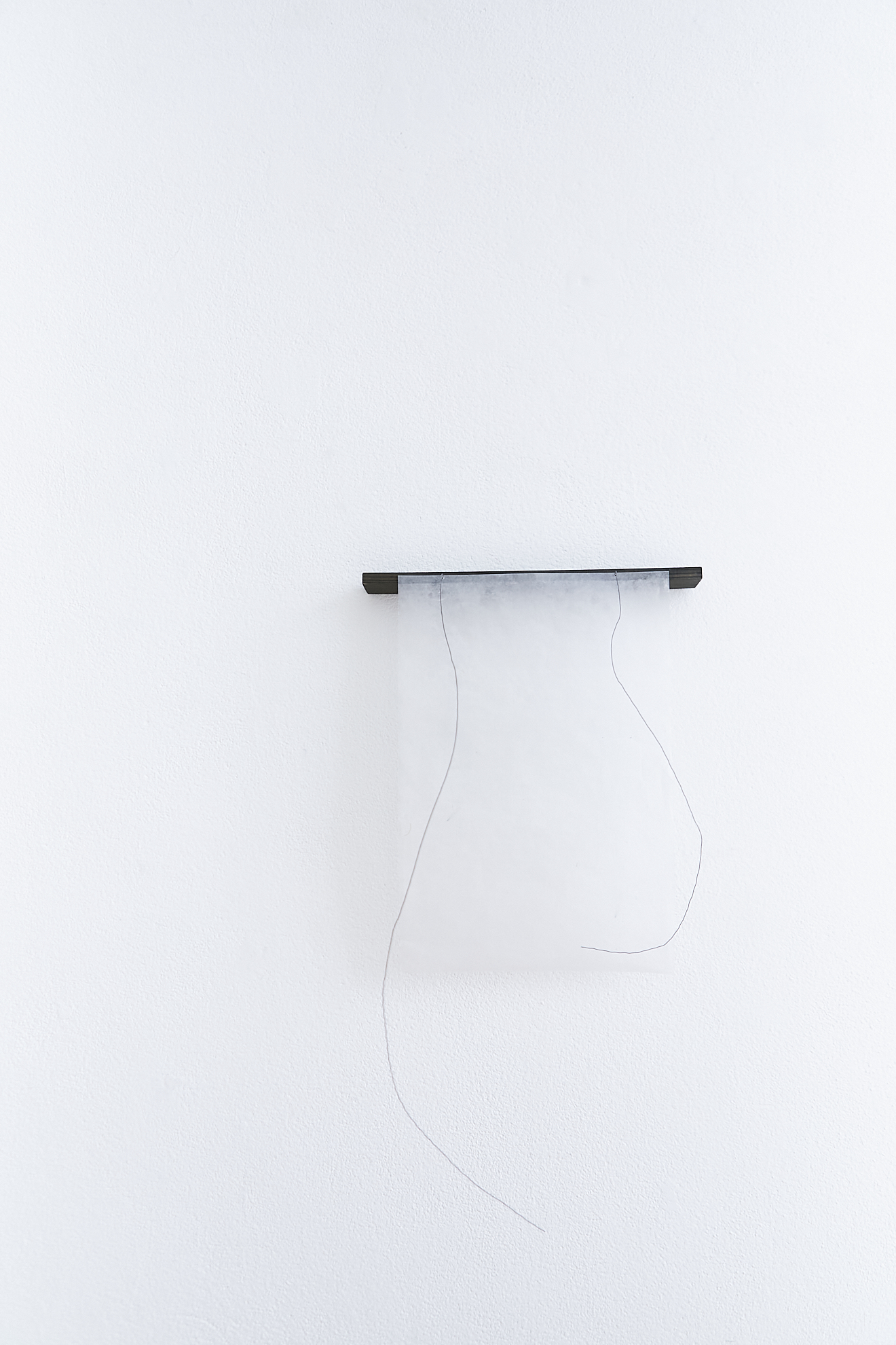 a black piece off wood with a transparent handmade paper over it is hanging off a white wall with two black wire lines hanging from the black wood